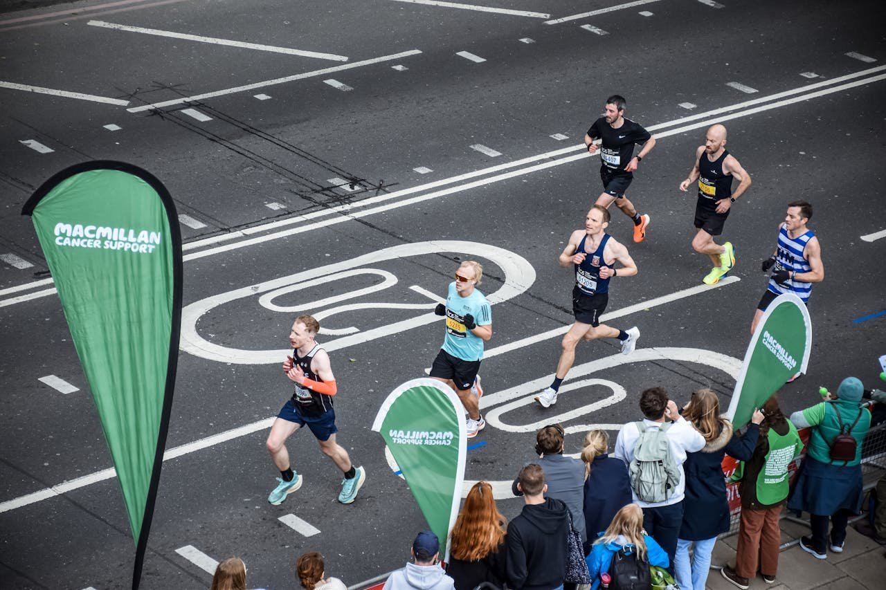 about-us-02 Runners participating in a marathon on London streets, viewed from above, with spectators cheering.